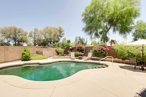 Piscina com borda curva, cercada por um muro de tijolos e diversas plantas.