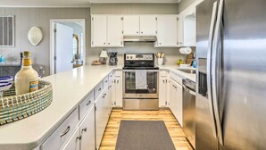 A modern kitchen with white cabinets, stainless steel appliances, and a wooden floor. - Waterfront Home w/ Decks, Privacy & Boat Slip (Supply)