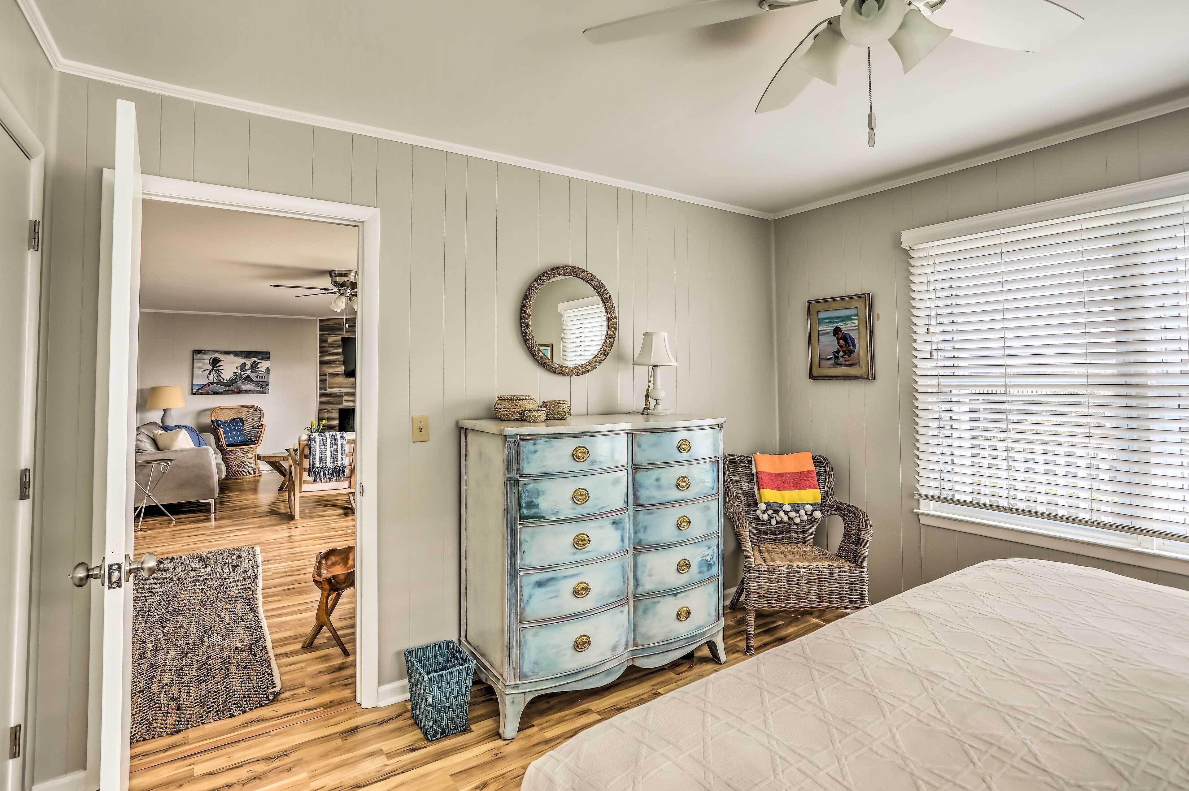 A bedroom with a bed, dresser, and a view of another room.