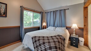 Ein Schlafzimmer mit einem Bett, zwei Nachttischlampen, einem Nachttisch, einem Mülleimer und einem Fenster mit Vorhängen.
