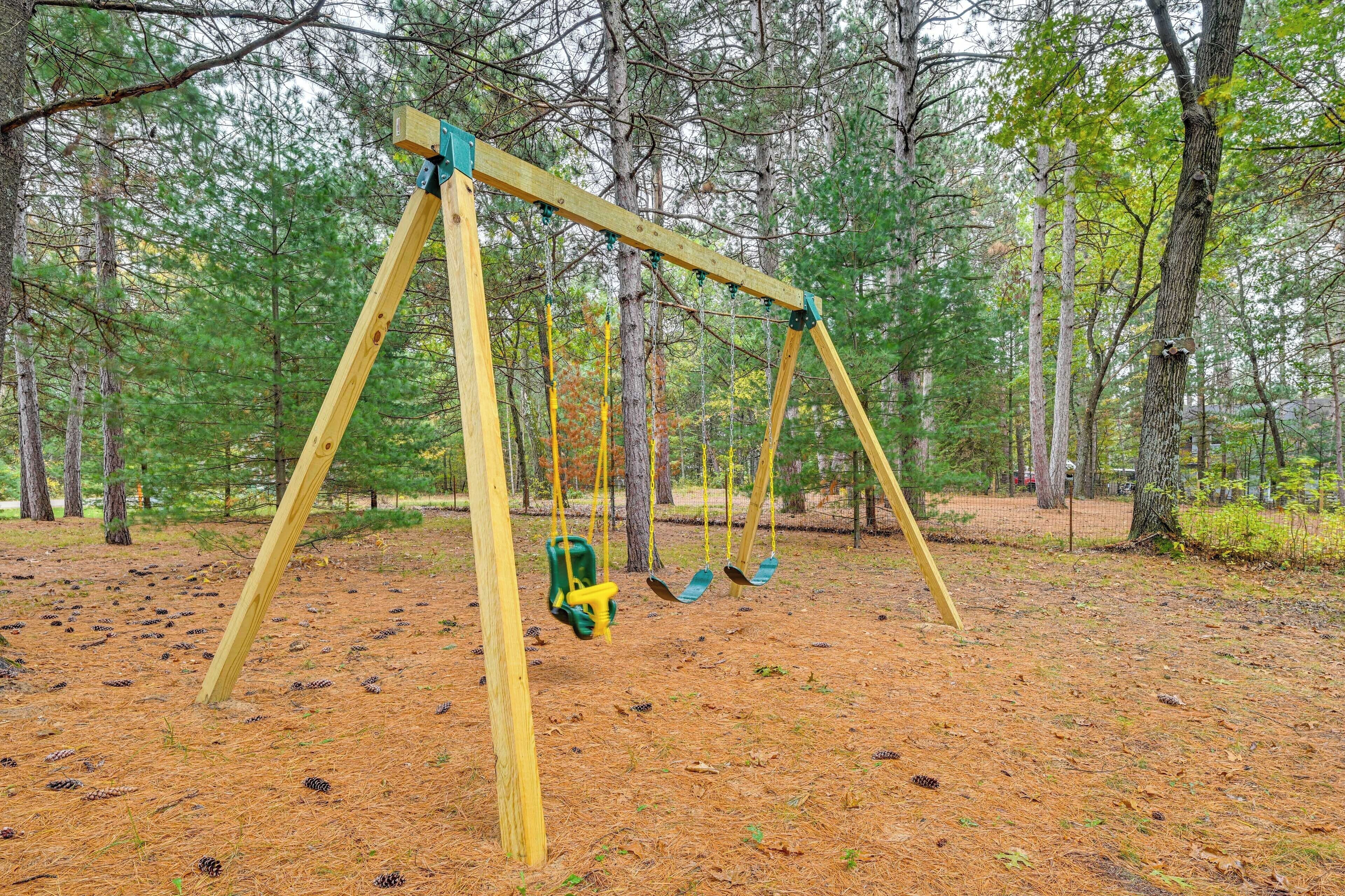 A wooden swing set in a forested area with pine trees and a ground covered in pine needles.