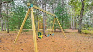 A wooden swing set in a forested area with pine trees and a ground covered in pine needles.