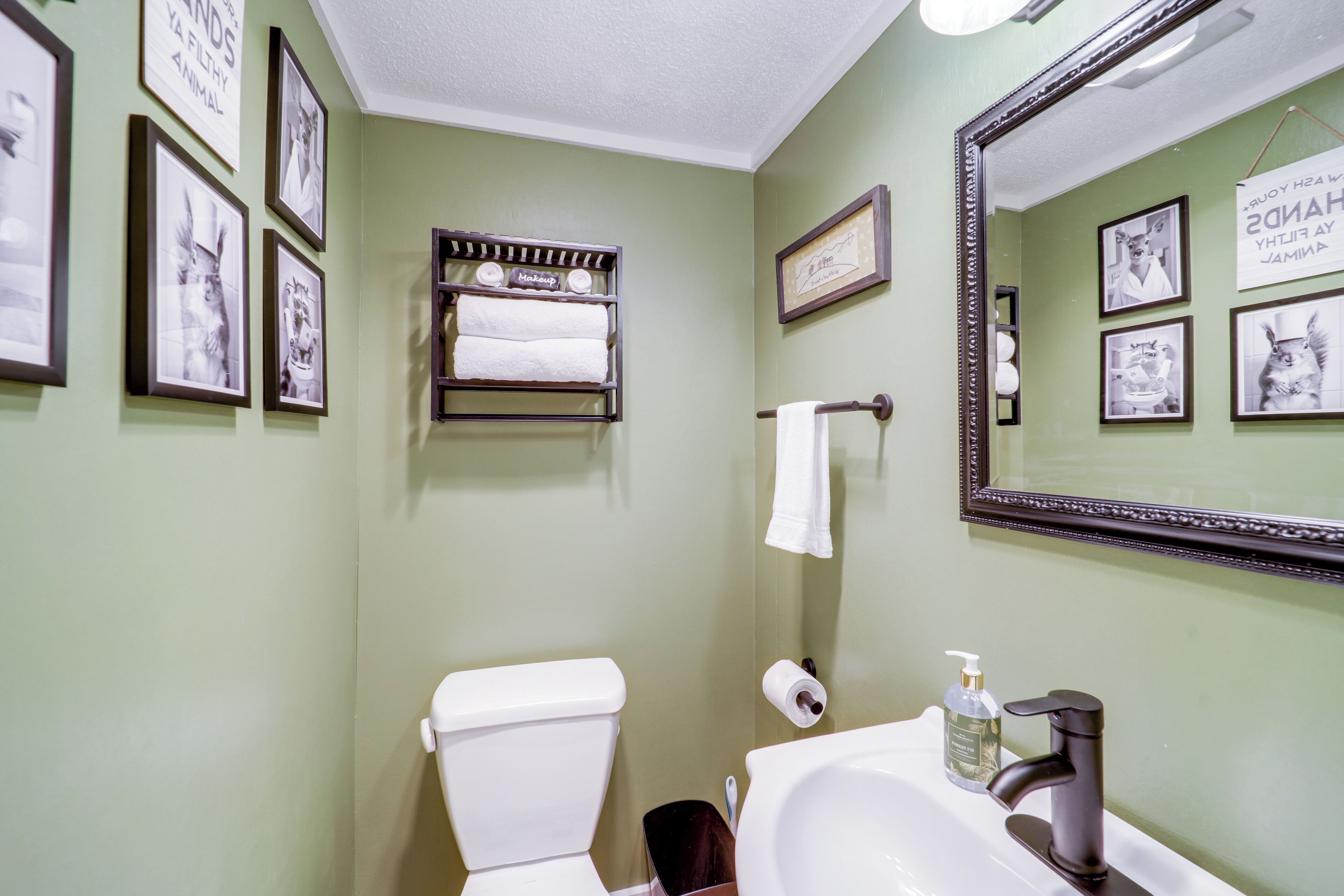 Une salle de bain avec des toilettes, un lavabo et un miroir. Des tableaux encadrés ornent le mur, et un porte-serviettes est placé au-dessus des toilettes.