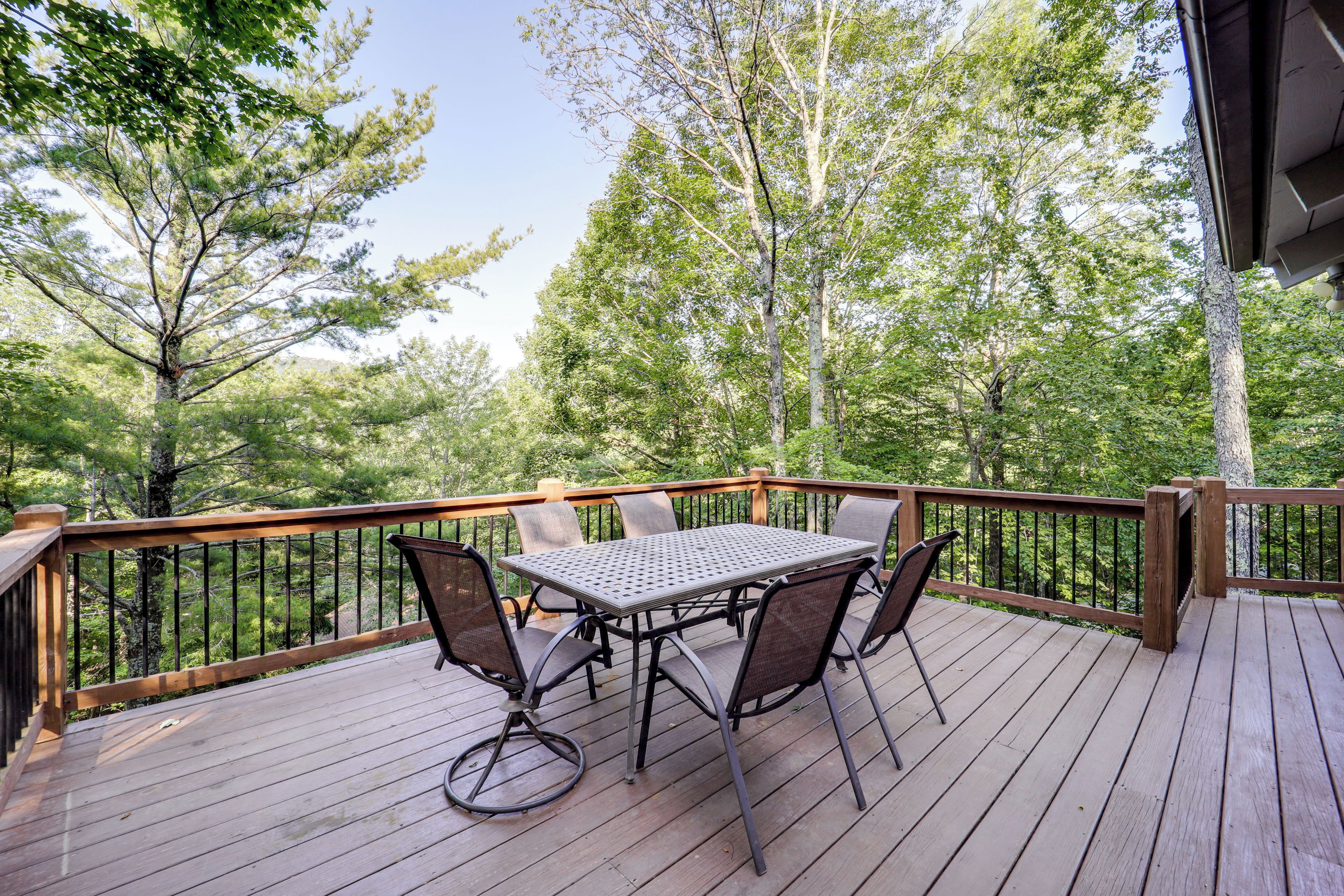 A wooden deck with a metal table and chairs, surrounded by trees.