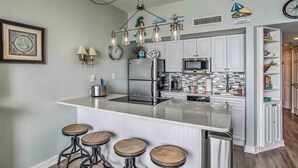 A modern kitchen with a central island, bar stools, stainless steel appliances, and decorative wall art. - Myrtle Beach Ocean-view Condo: Walk to Beach! (Myrtle Beach)