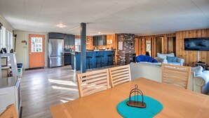 A spacious living area with a wooden dining table, kitchen, and a TV mounted on the wall. - Updated Bristol Lakehouse w/ Kayaks & Beach Access (Bristol)