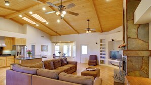 A spacious living area with a wooden ceiling, a large sofa, a television, and a stone fireplace. - Luxe Scottsdale Home w/ Horse Stables & Pool! (Scottsdale)