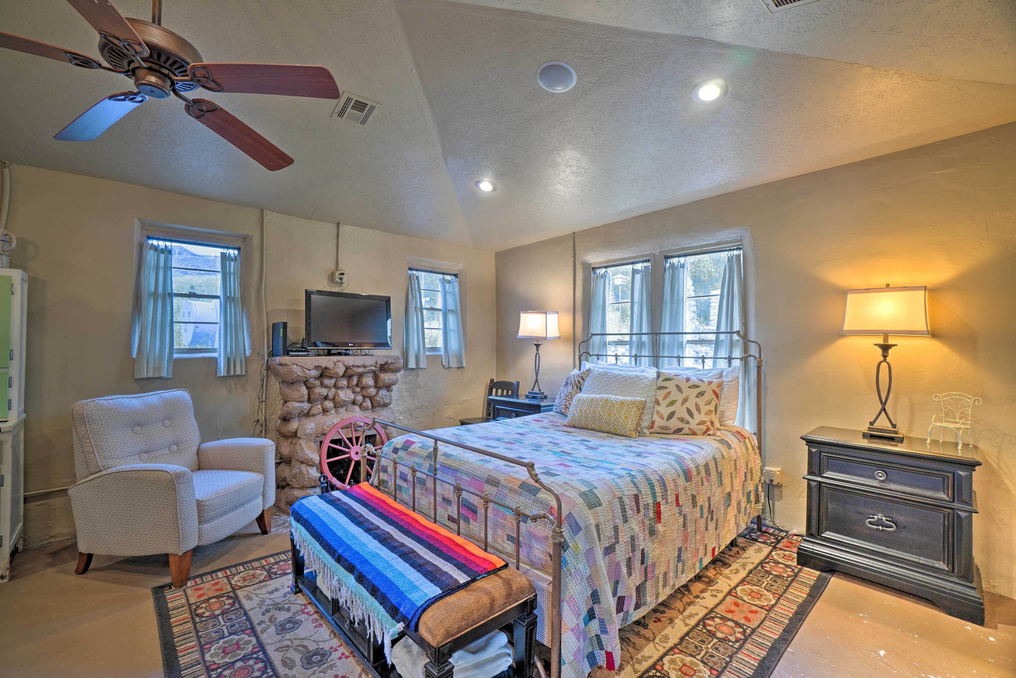 A bedroom with a bed, a chair, a bench, a nightstand, a lamp, a television, and a ceiling fan.
