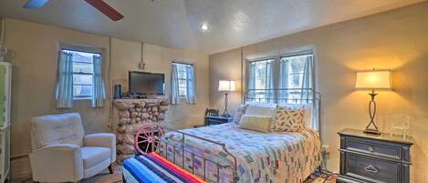 A bedroom with a bed, a chair, a bench, a nightstand, a lamp, a television, and a ceiling fan.