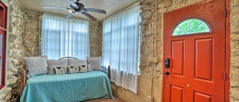 Una habitación con cama, ventilador de techo y puerta roja.
