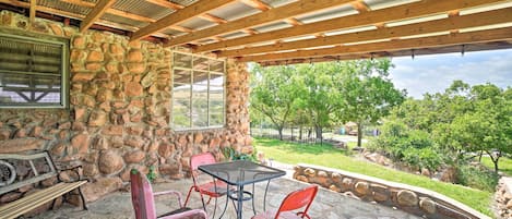 Un patio cubierto con muros de piedra, techo de madera y vista a un jardín ajardinado.