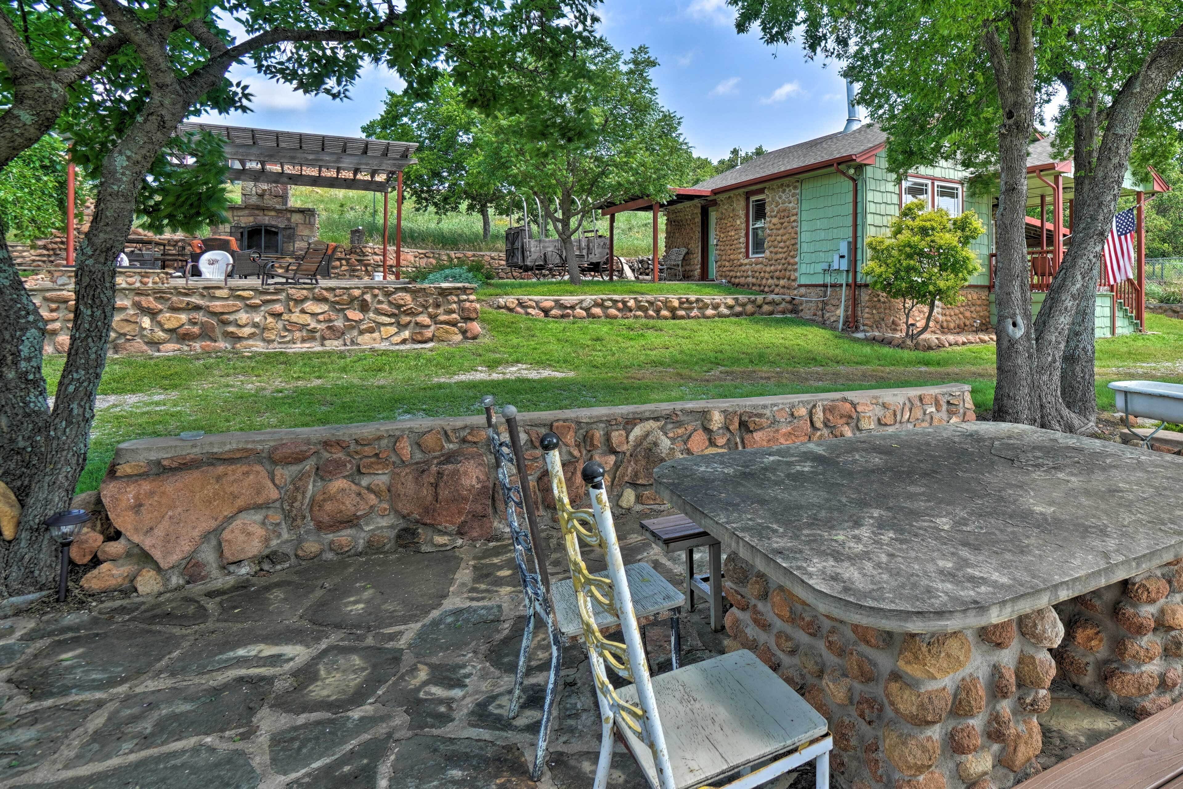 A stone patio with outdoor seating, a stone fireplace, and a covered area with a grill.