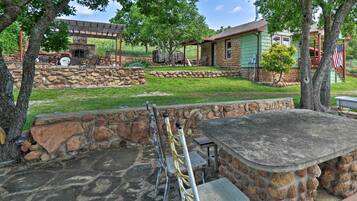 A stone patio with outdoor seating, a stone fireplace, and a covered area with a grill.