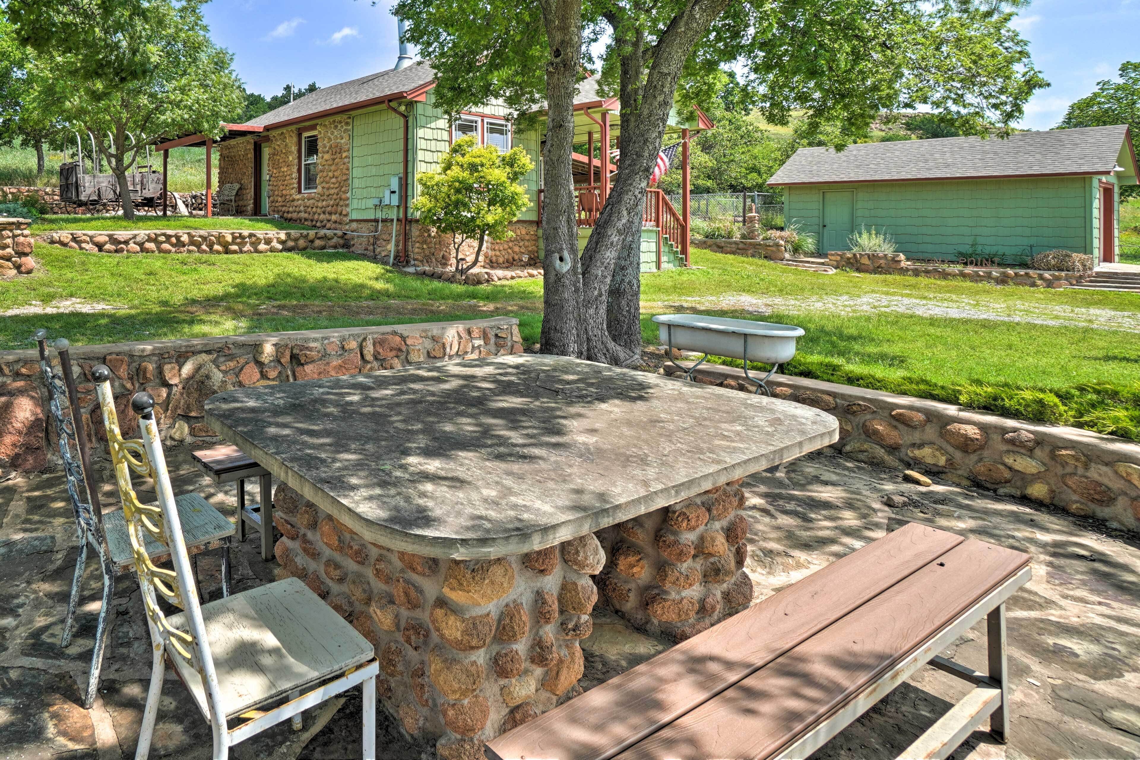 Une terrasse en pierre avec une table et des bancs, entourée d’un muret en pierre et d’un petit arbre.