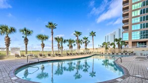 A swimming pool with palm trees and lounge chairs, surrounded by a brick patio. - Ocean Views & Pool Access: Orange Beach Condo! (Orange Beach)