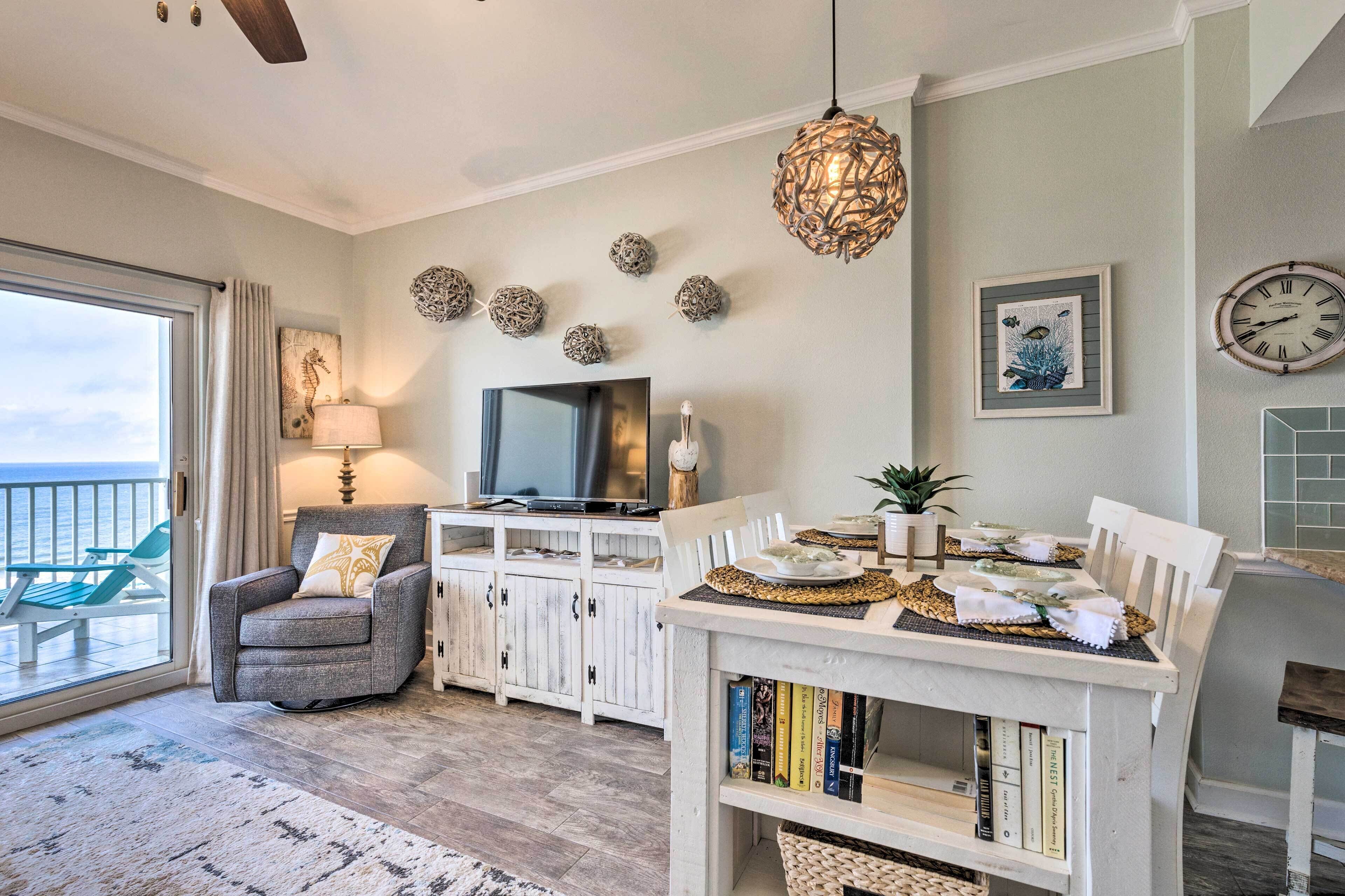 A cozy living room with a TV, white cabinets, a dining table set, and a balcony with a view.