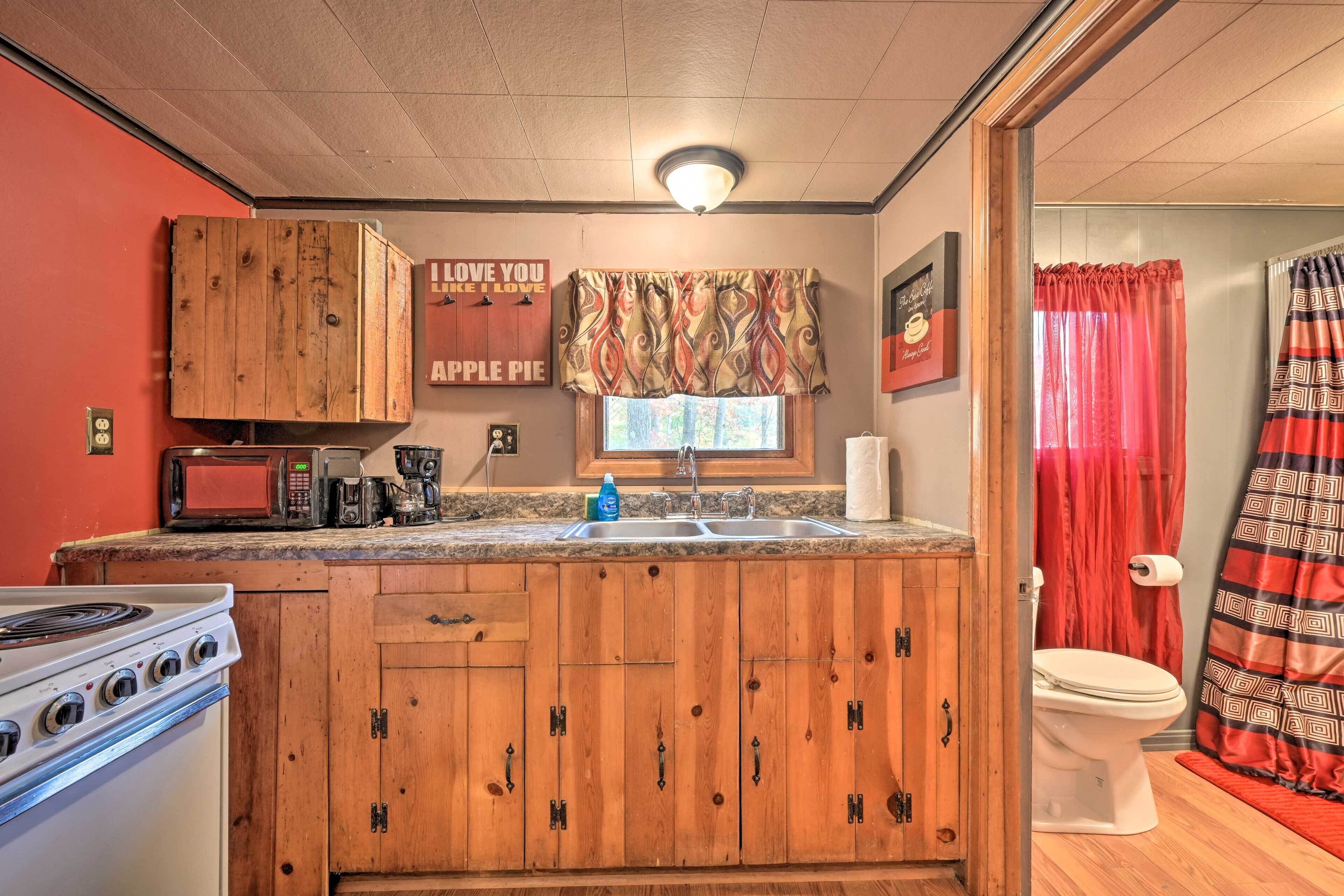 A compact kitchen with wooden cabinets, a microwave, a stove, and a window with curtains.