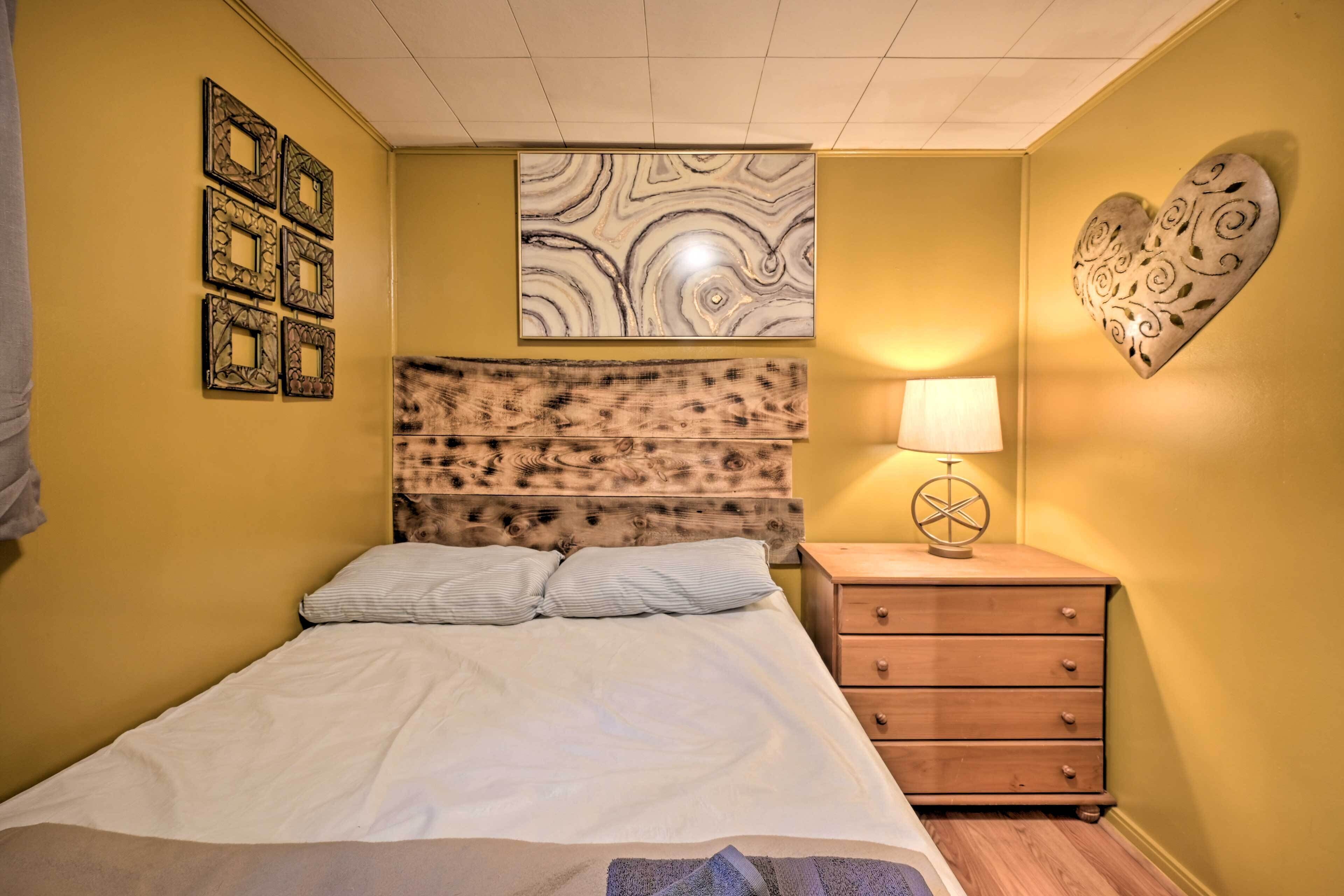 A bedroom with a bed, a wooden headboard, a bedside table with a lamp, and decorative wall art.