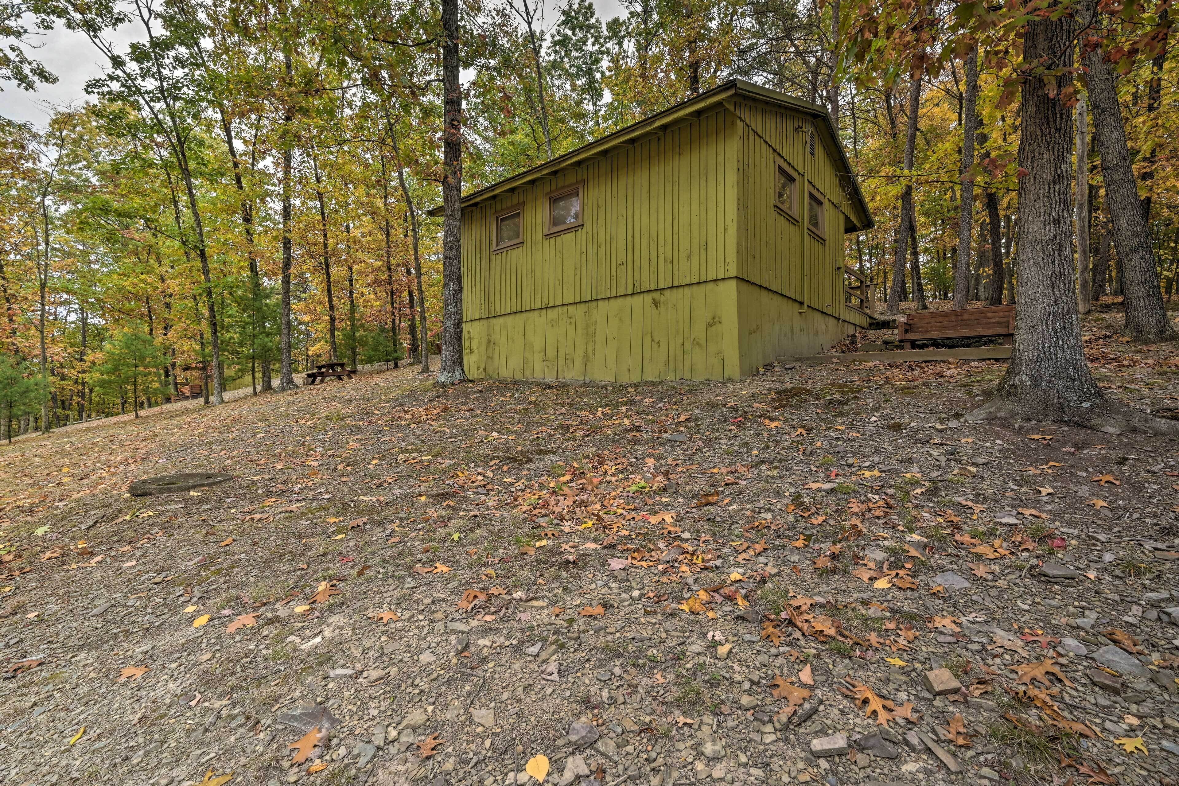 A rustic cabin with a simple design, surrounded by a forest with autumn-colored leaves.
