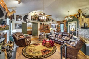 A cozy living room with leather furniture, a fireplace, and various wall decorations including animal mounts and a chandelier. - 2 Mi to Gatlinburg Strip: Serene Cabin w/ Hot Tub! (Gatlinburg)