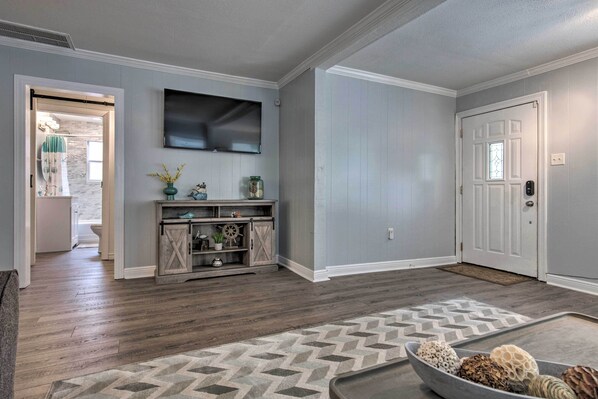 A living room with a wooden floor, a patterned rug, a television on the wall, and a door with a window. - Gulfport Bungalow by Jones Park/beach Access! (Gulfport)