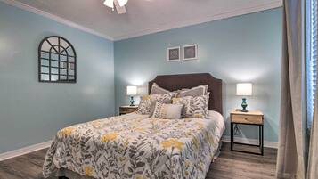 A bedroom with a bed, two bedside tables, a ceiling fan, and a window with a decorative frame.