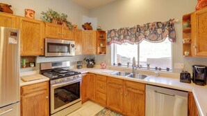 A kitchen with wooden cabinets, stainless steel appliances, a window with patterned curtains, and a sink. - Desert Gem w/ Patio + Grill, Near Oracle St. Park! (Oracle)