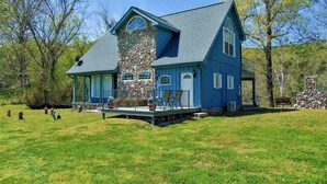 A large blue house with a stone tower, a covered porch, and a stone fireplace. - Rubys Landing Cottage w/ Deck & White River Views (Melbourne)