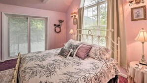 A bedroom with a large bed, a window with curtains, a bedside table with a lamp, and a wall-mounted light fixture. - Rubys Landing Cottage w/ Deck & White River Views (Melbourne)