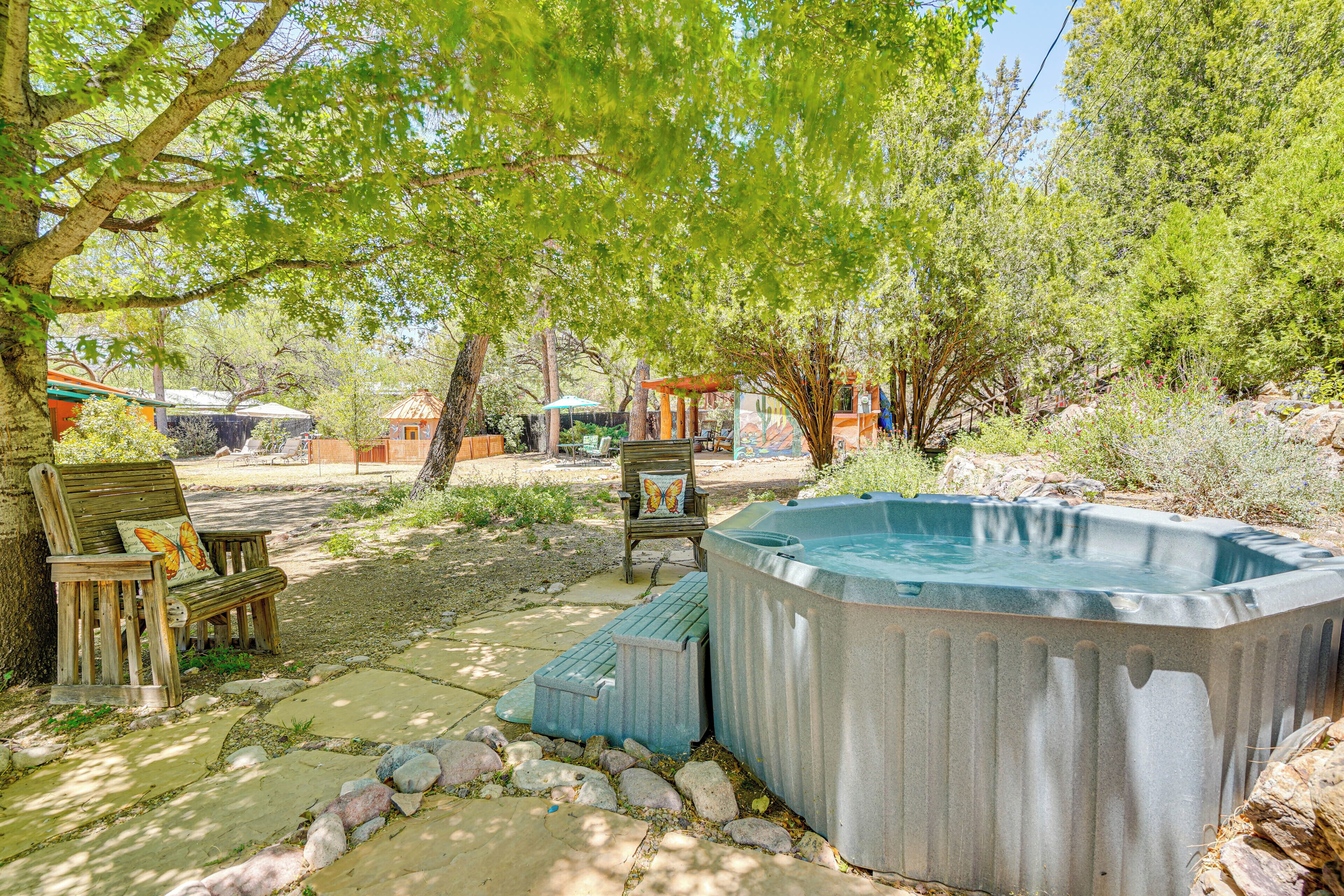 A hot tub surrounded by a stone pathway, wooden benches, and a butterfly cushion.