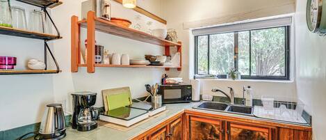 A kitchen with wooden cabinets, a coffee maker, a microwave, and a window with a view of trees.