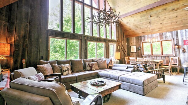 A rustic cabin interior with a large wooden ceiling, a chandelier, and a cozy seating area with a sofa and chairs. - East Burke House w/ Deck < 3 Mi to Kingdom Trails! (East Burke)