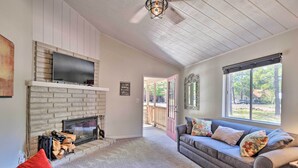 A living room with a fireplace, a sofa, a TV, and a large window. - Coconino National Forest Home W/deck & Yard! (Munds Park)