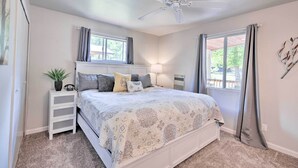 A bedroom with a bed, bedside table, lamp, ceiling fan, and windows with curtains. - Coconino National Forest Home W/deck & Yard! (Munds Park)