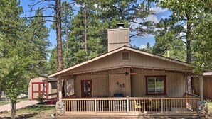 A wooden cabin with a porch, a chimney, and a small attached building with a red door. - Coconino National Forest Home W/deck & Yard! (Munds Park)