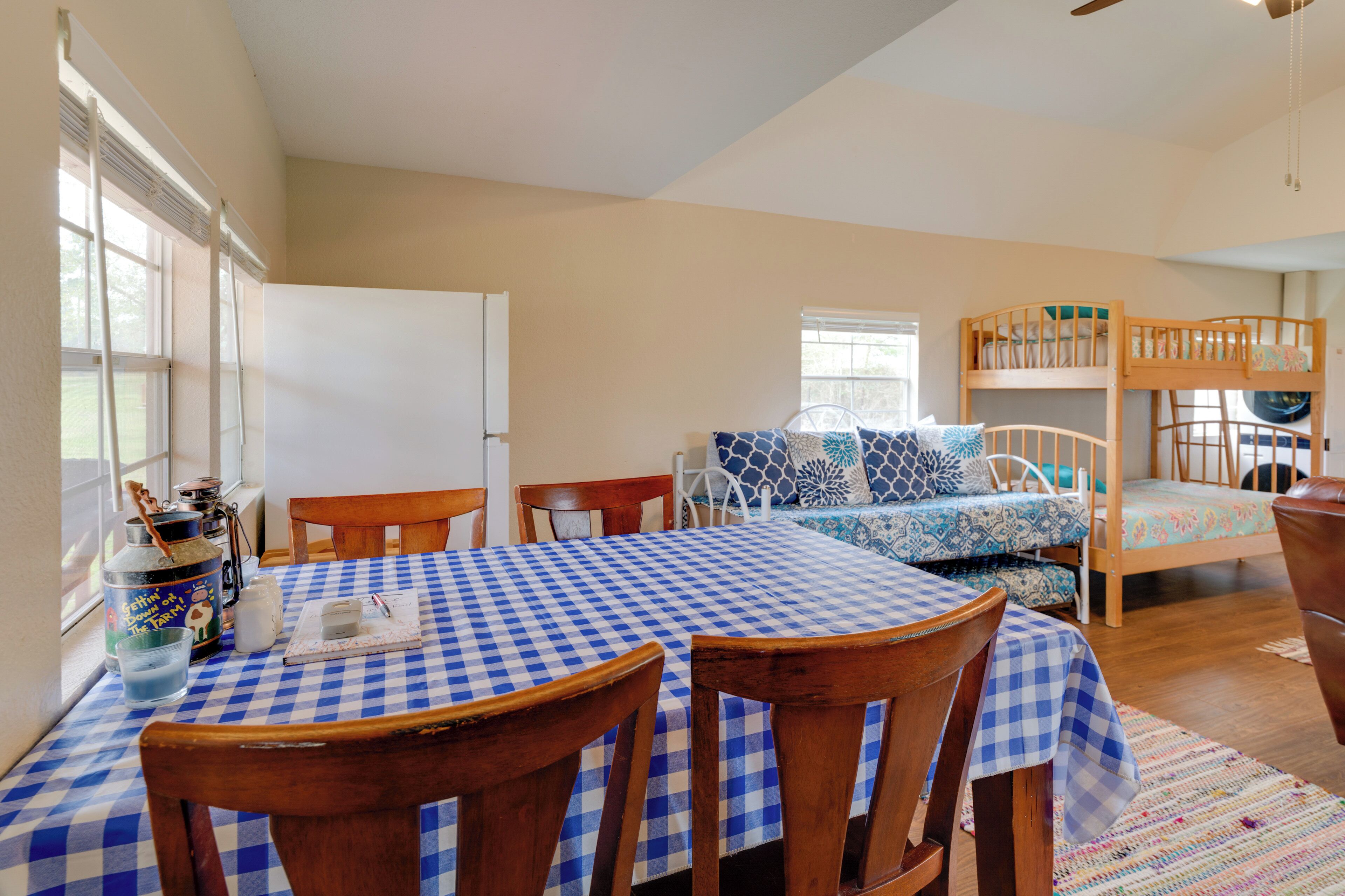 A room with a checkered table, bunk beds, a refrigerator, and a window with blinds.