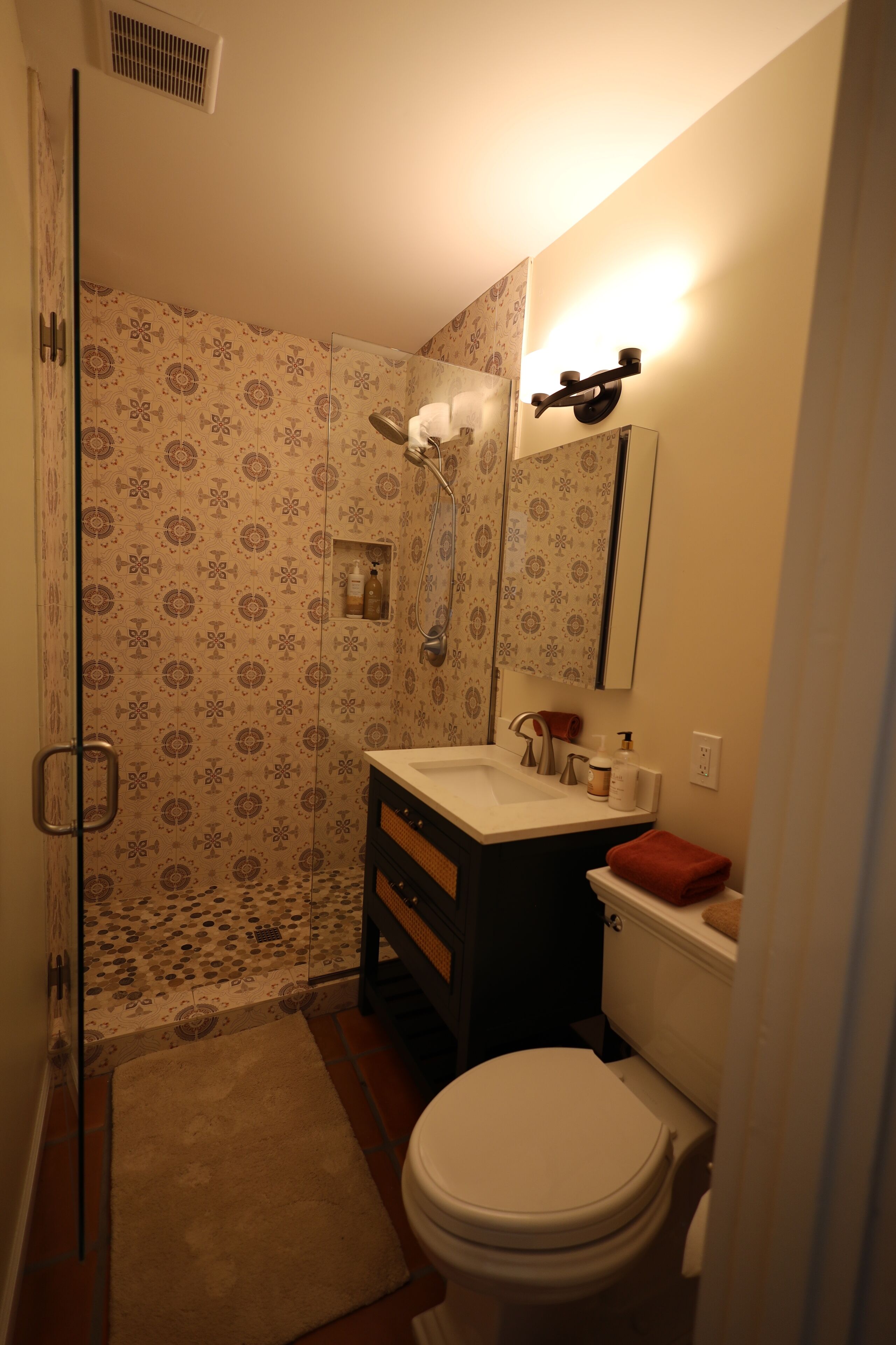 A bathroom with a shower, toilet, sink, and a mirror.