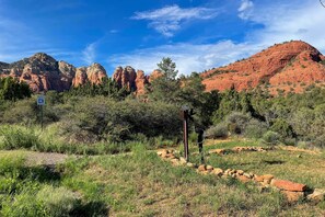 A natural landscape with red rock formations, green vegetation, and a clear blue sky.