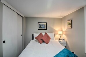 A neatly made bed with white and pink pillows, a bedside lamp, and a framed picture on the wall. - Fresh Downtown Longmont Apartment - Walk to Main! (Longmont)