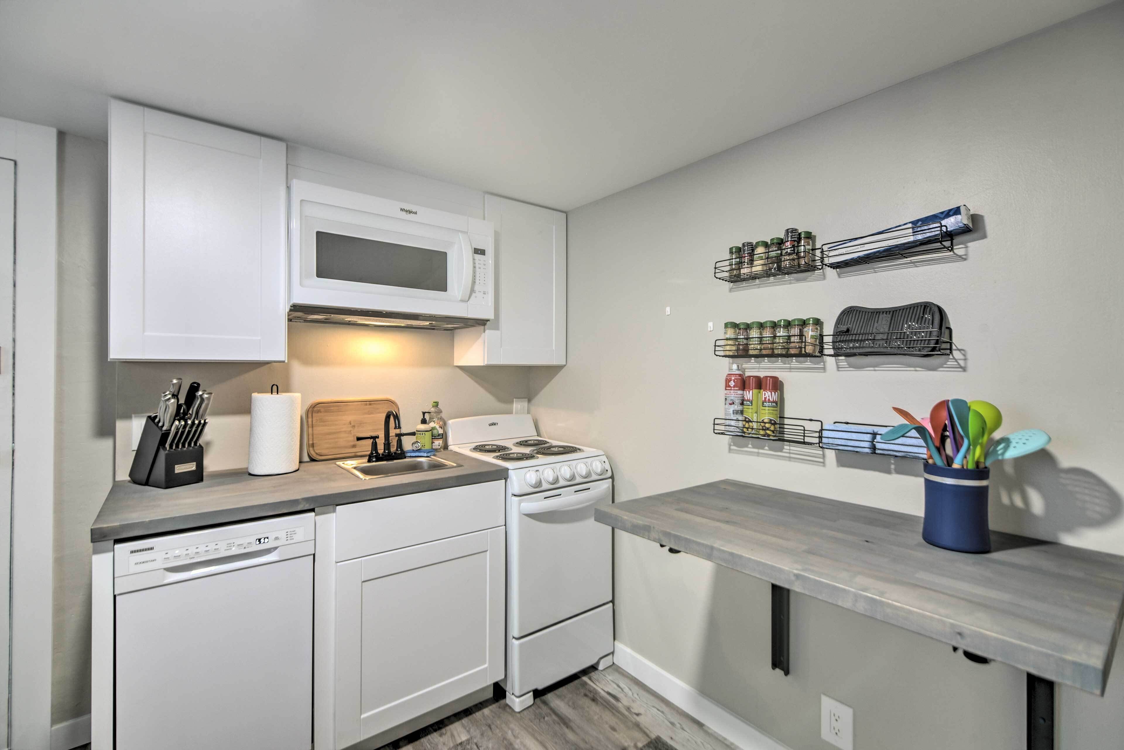 A compact kitchen with white cabinetry, a microwave, a stove, and a countertop with various kitchen items.