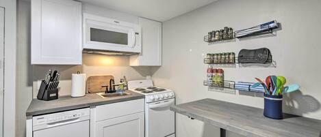 A compact kitchen with white cabinetry, a microwave, a stove, and a countertop with various kitchen items.