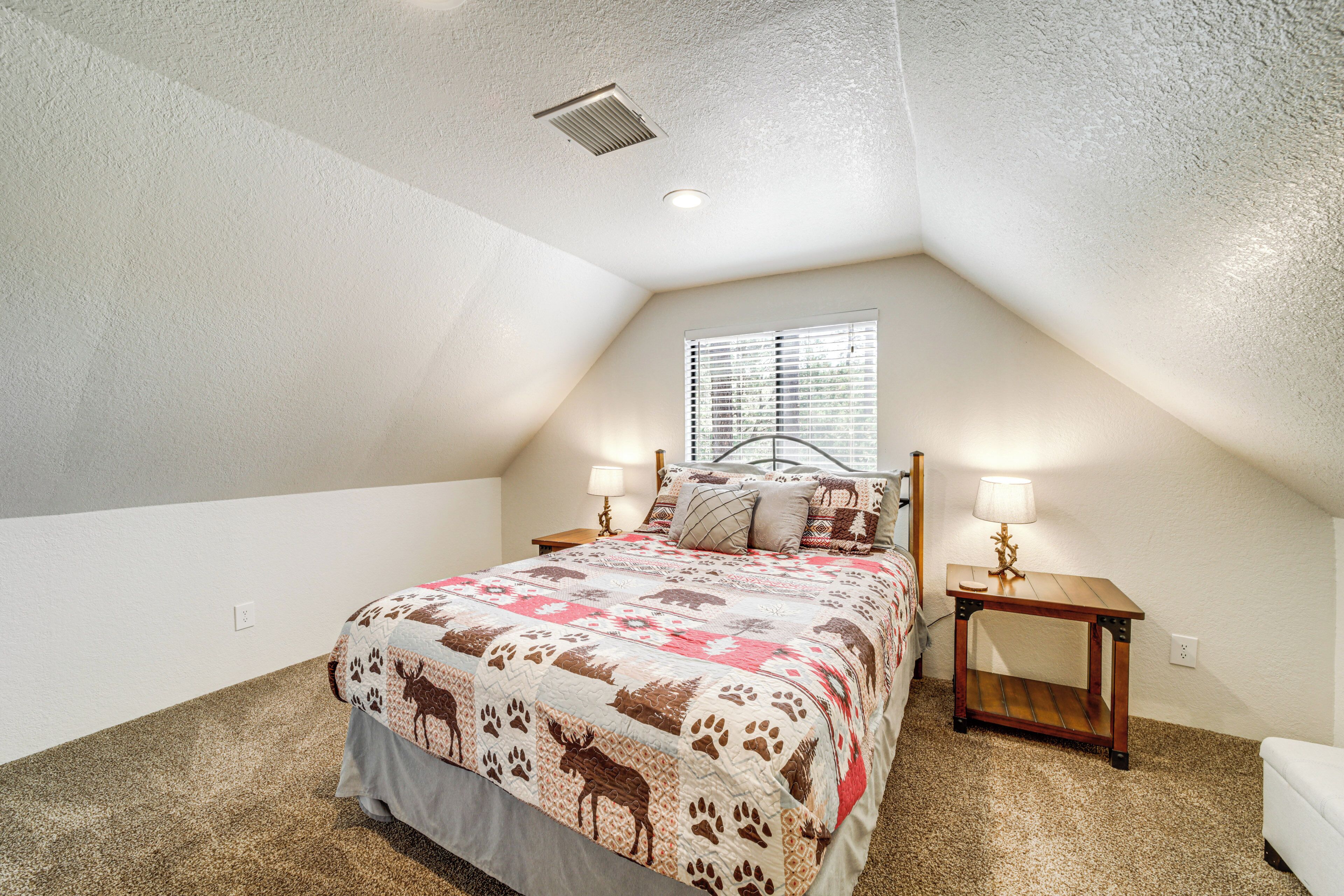 A bedroom with a large bed, two bedside tables, a window, and a ceiling vent.