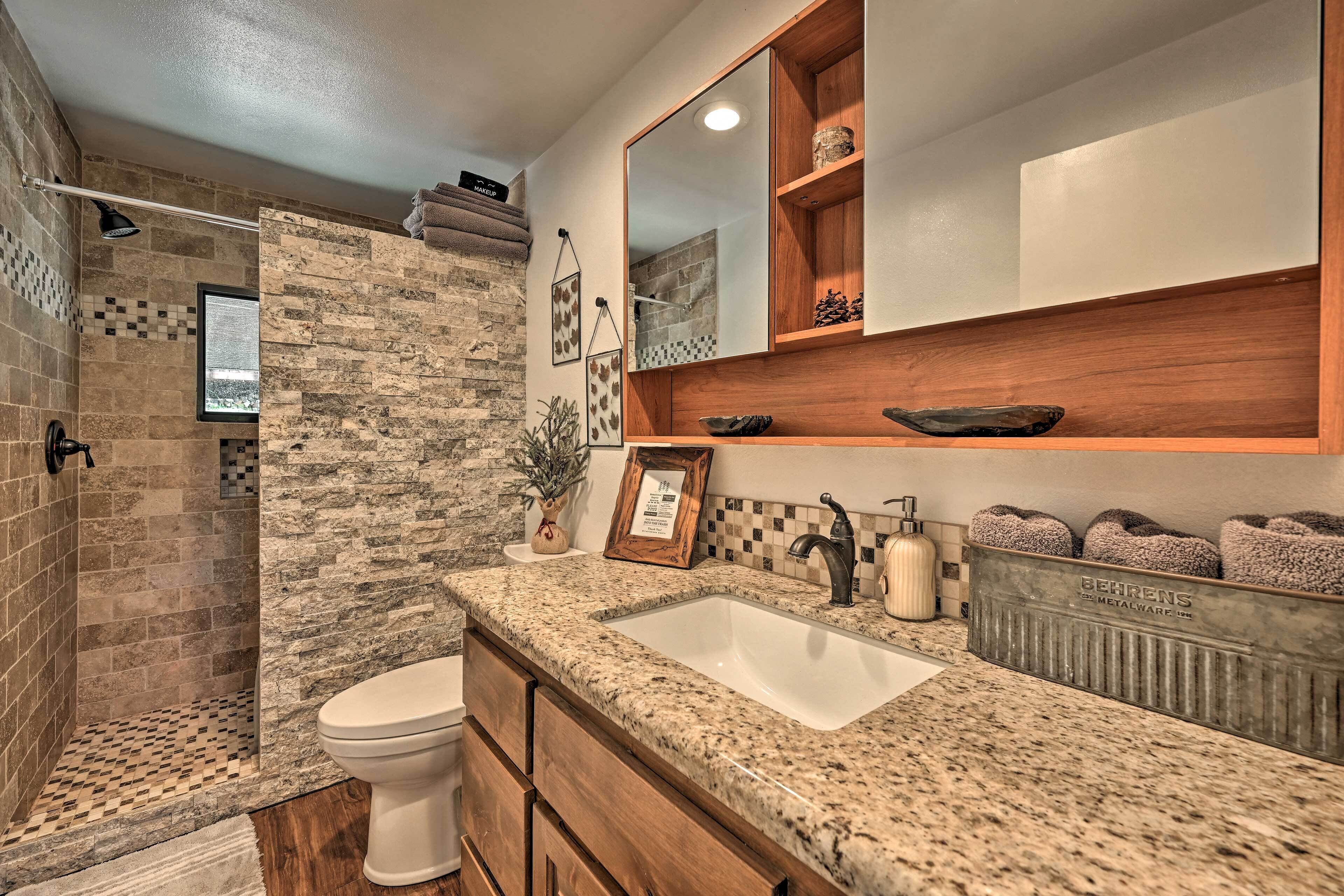 A bathroom with a stone shower, a sink with a wooden vanity, and a mirror above the vanity.