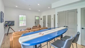 A modern living room with a large blue surfboard-shaped coffee table, leather sofas, and a TV on a tripod. - Rural Family Retreat < 3 Mi to Fishing & Boating! (Higden)