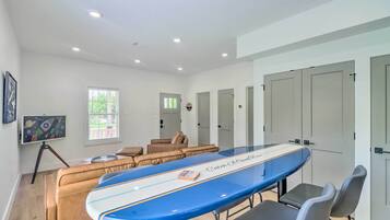 Un salon moderne avec une grande table basse en forme de planche de surf bleue, des canapés en cuir et un téléviseur posé sur un trépied.