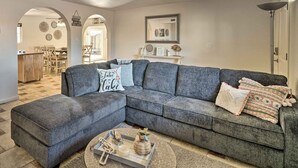 A living room with a grey sectional sofa, a coffee table, and decorative pillows. There is a dining area visible in the background. - 5 Mi to Marina: Lake Havasu City Home w/ Pool! (Lake Havasu City)
