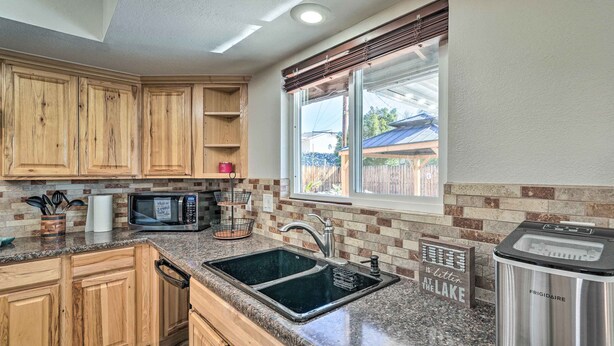 A kitchen with wooden cabinets, a granite countertop, a stainless steel sink, a microwave, and a refrigerator. - 5 Mi to Marina: Lake Havasu City Home w/ Pool! (Lake Havasu City)