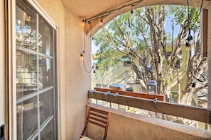 A balcony with a wooden bench, a window with a view of trees and buildings, and string lights. - Bright Burbank Condo < 2 Mi to Griffith Park! (Burbank)