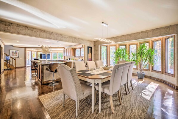 A spacious dining area with a central island, large windows, and a modern kitchen in the background.