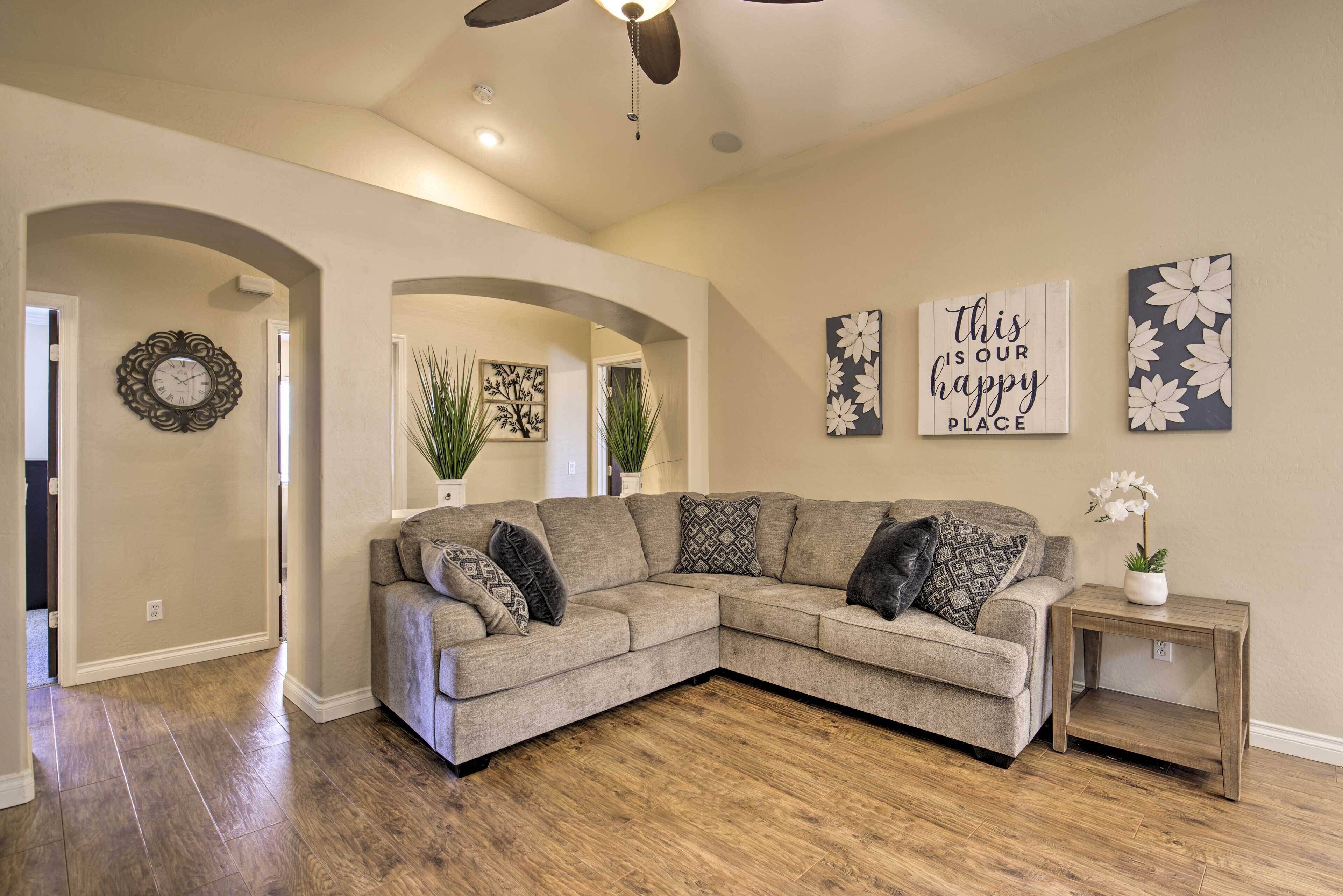 A living room with a sectional sofa, decorative wall art, and a ceiling fan.